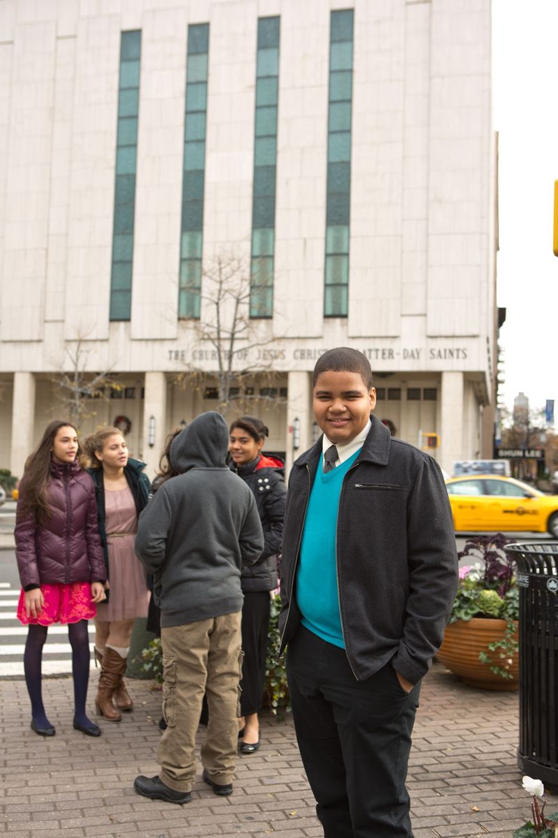 A young man stands in front of the Manhattan New York Temple and smiles.
