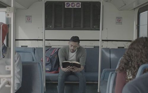 A man sits on a bus reading and studying the Book of Mormon