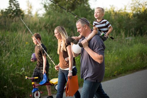 A mother and father take their two sons on a fishing trip, carrying fishing tackle and poles.