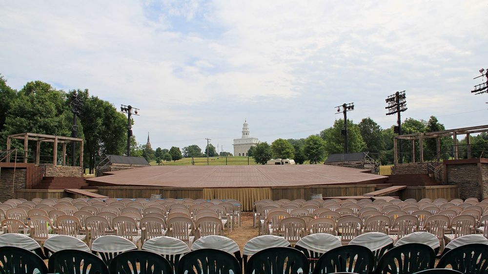 View of a wooden stage from behind multiple rows of plastic chairs.