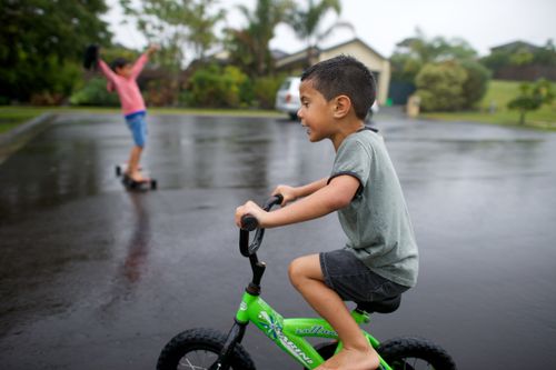 A little boy from New Zealand rides on his green bike through the rain.