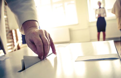 A woman's hand putting a ballot into a ballot box.