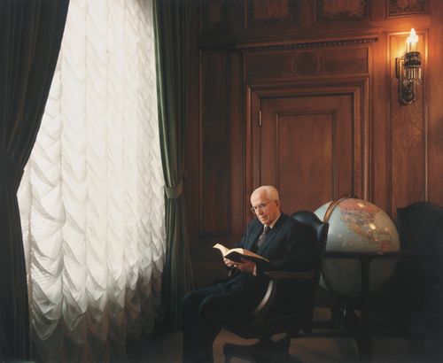 President Benson sitting near a tall window, reading scriptures, with a globe behind him.