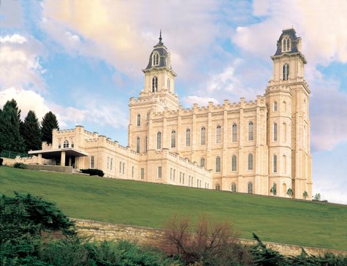 A side view of the Manti Utah Temple on a green hill, with pink and orange clouds overhead.