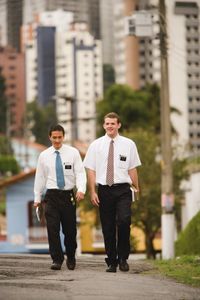 Two elder missionaries walking down a city sidewalk in Sao Paulo, Brazil.  There are buildings in the background.