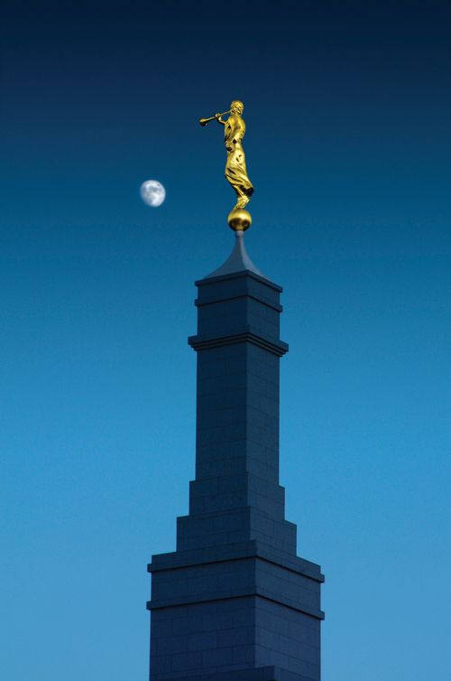 The spire of the Fresno California Temple and the angel Moroni at nighttime, with the moon on the left side.