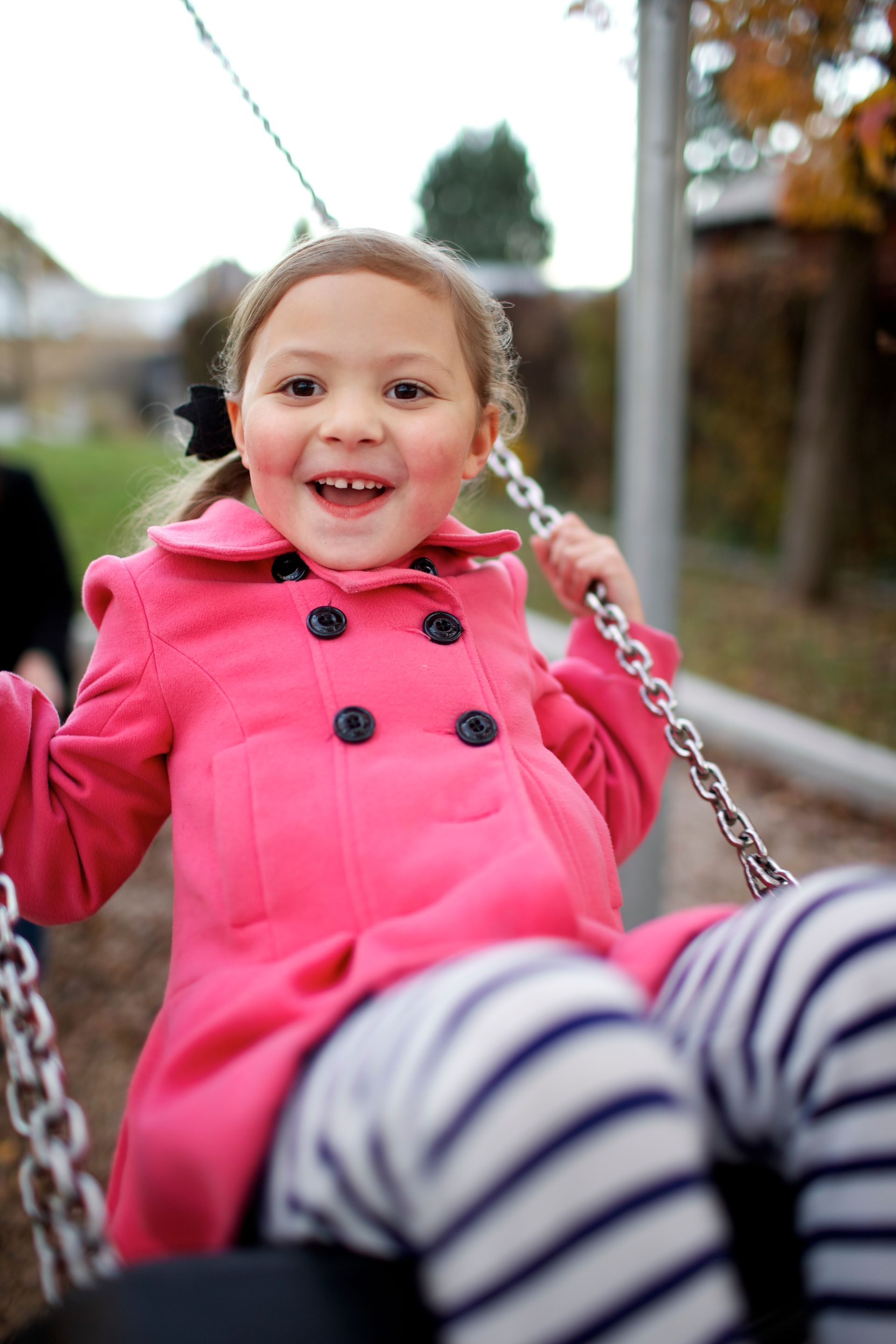 A girl in a pink coat plays on a swing.