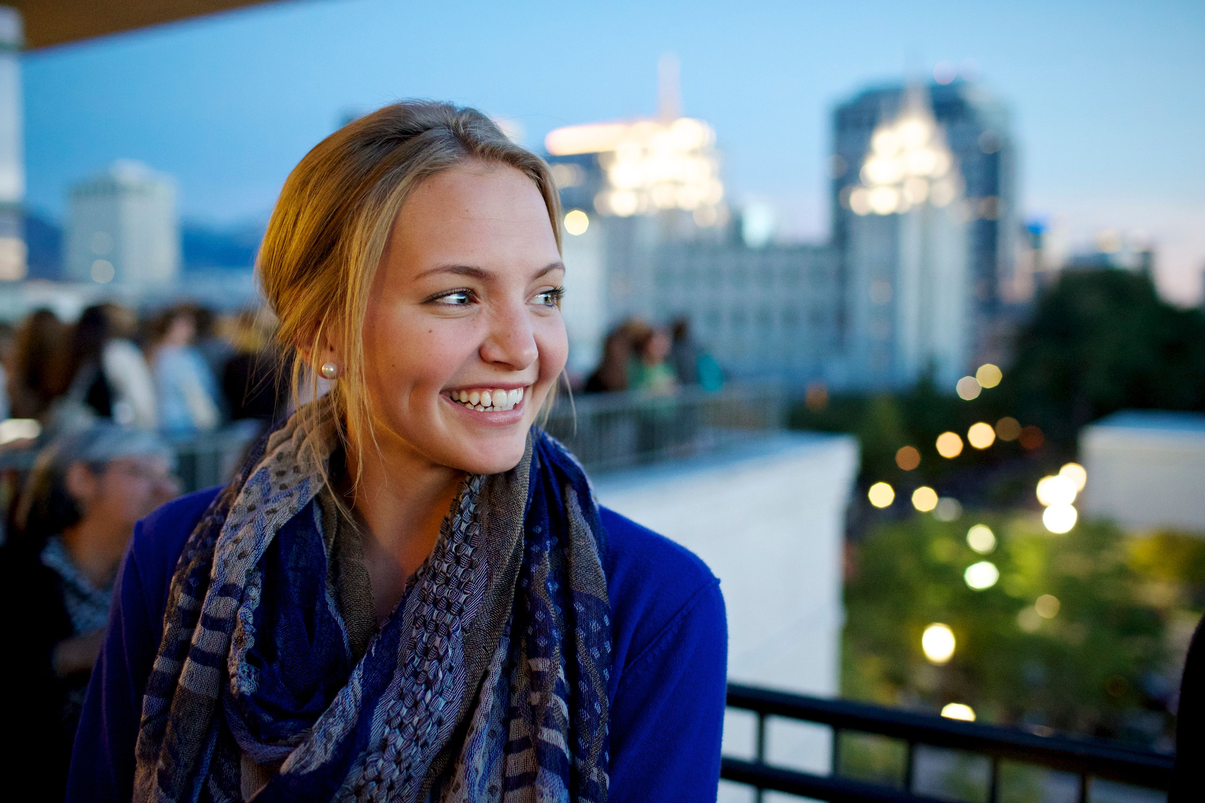 A young woman standing on a balcony with the Salt Lake Temple in the distance.