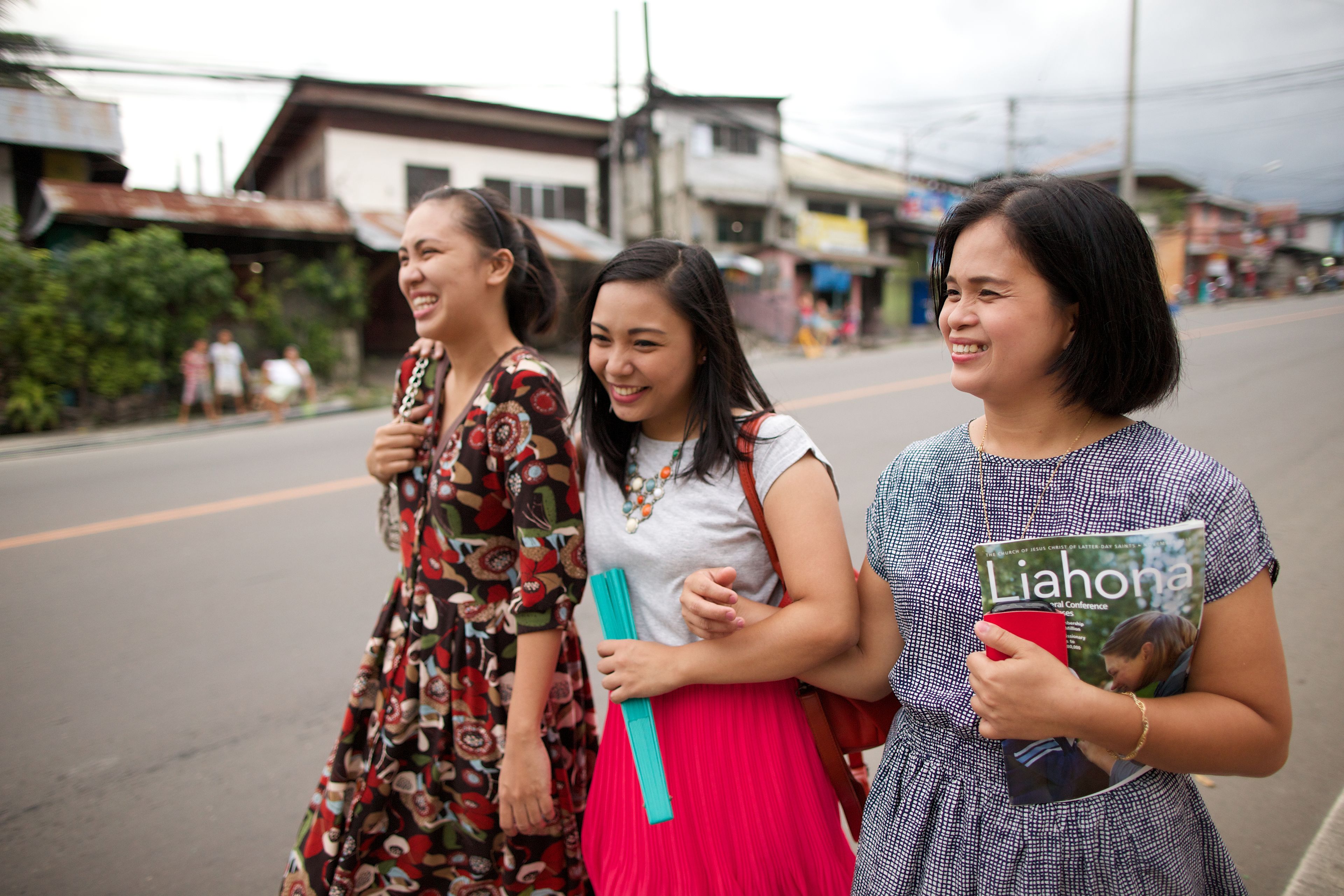Three young women from the Philippines, wearing dresses and skirts, walking down the street.