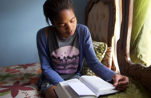 a young woman sitting on her bed and reading the scriptures