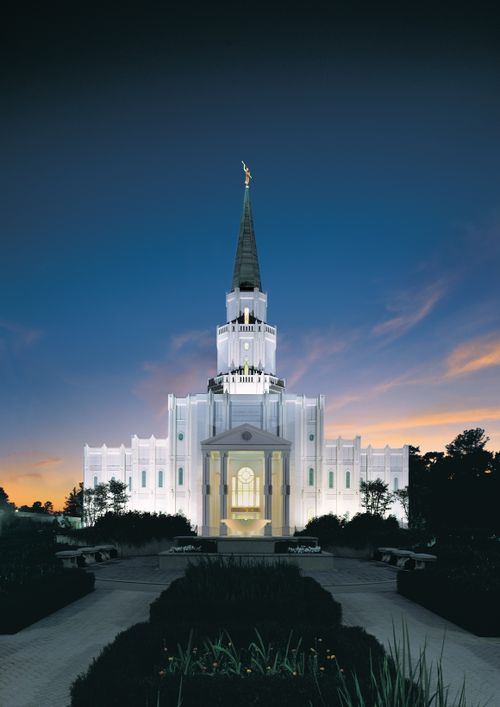 The front of the Houston Texas Temple from afar at night, with all of the lights on inside and outside and a dark blue sky beyond.