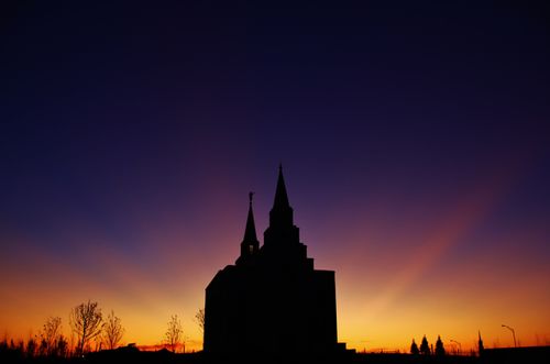 A silhouetted image of the Kansas City Missouri Temple, with the orange and purple colors of the sunset in the background.