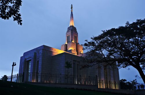 The Cebu City Philippines Temple in the evening, with the lights on in the spire and a large tree on the right-hand side.