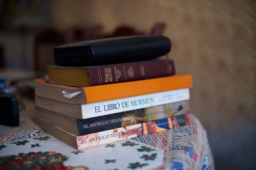 A stack of Spanish books, including scriptures and other study materials, lying on a tablecloth.