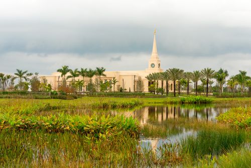 The Fort Lauderdale Florida Temple from afar, with a pool of water reflecting the temple’s image amidst green grass.