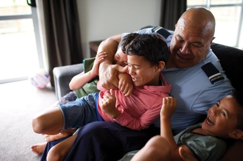 A man sitting on a couch and playing with his three grandsons.