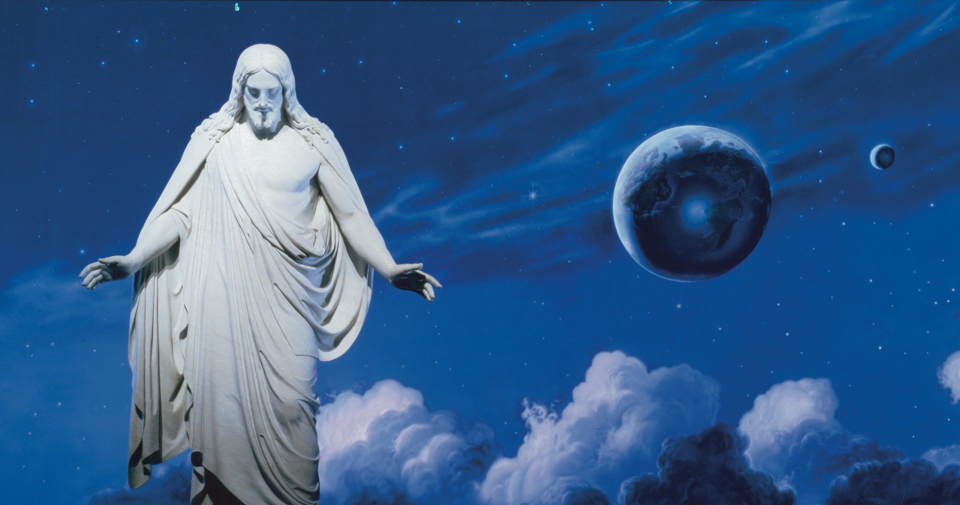 The resurrected Jesus Christ standing with His arms slightly extended. The wounds of the Crucifixion are visible in the hands, feet and side of Christ.  The "Universe" mural by Sidney King is visible behind the Christus statue.