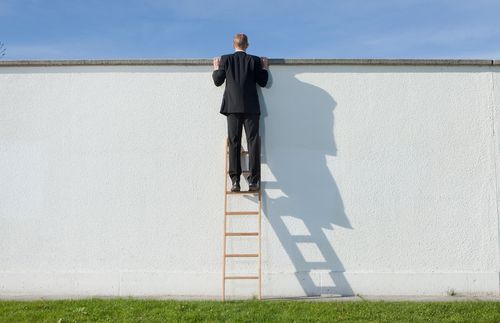 young man staning on a ladder and looking over a wall