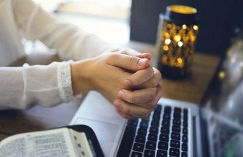 hands clasped in prayer by a computer
