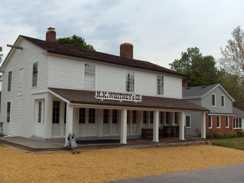 A front exterior view of the Newel K. Whitney store, made of white wood with black shingles.