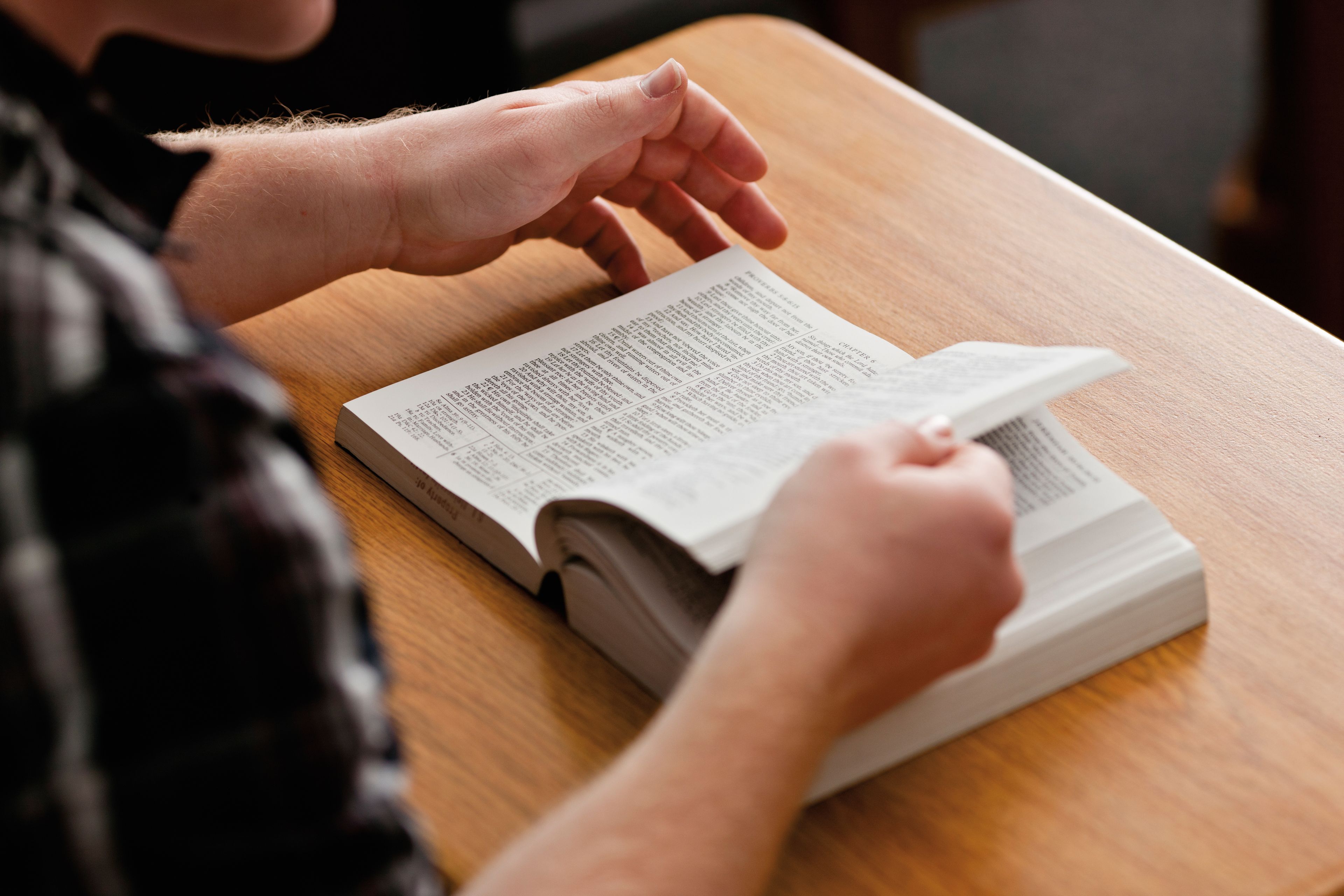 Hands flipping through the pages of a Bible on a desk.