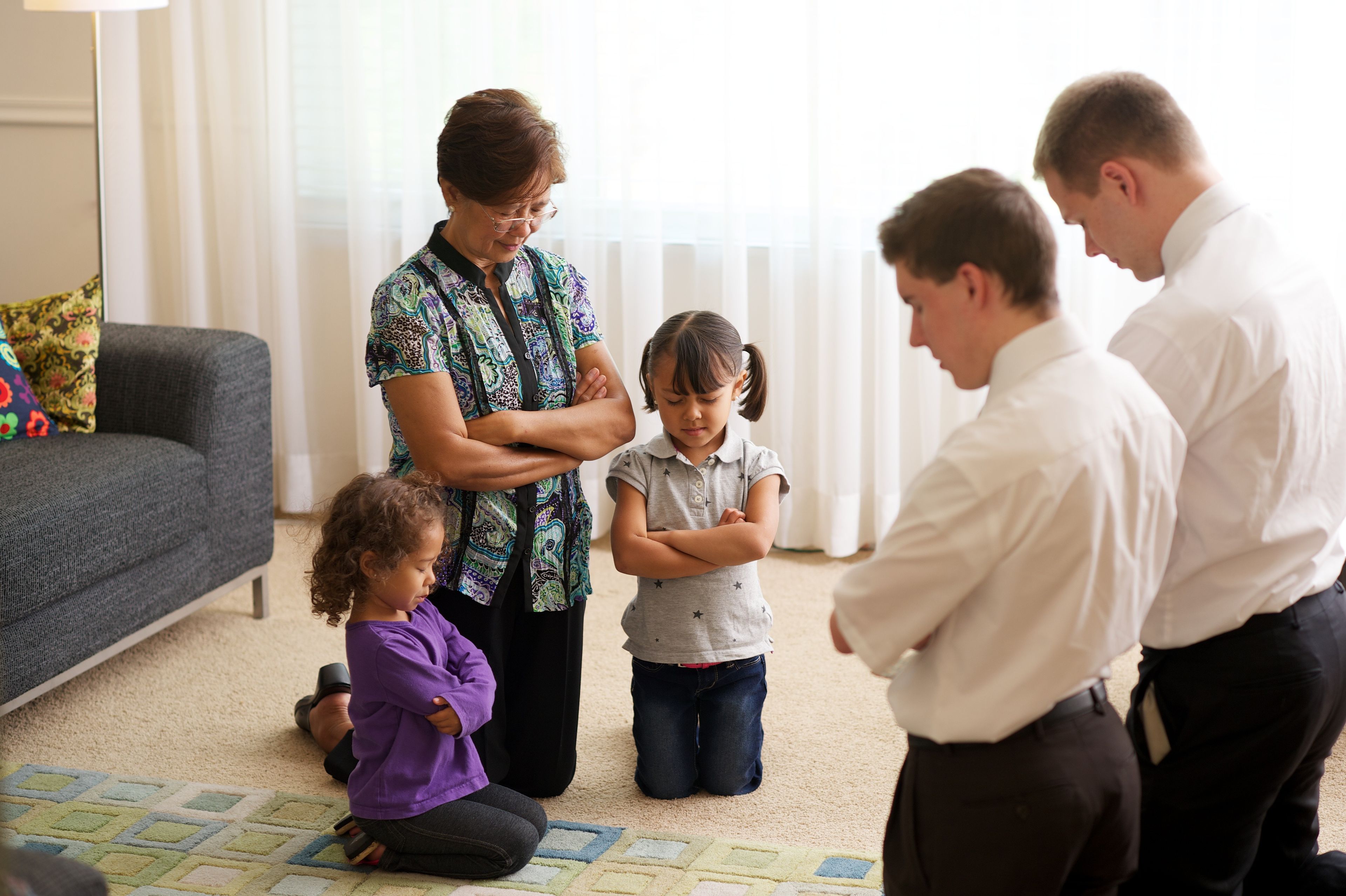 Missionaries pray with a grandmother and her two granddaughters.