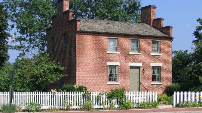 Brick home with white picket fence, brick sidewalk, and pink-flowering trees.