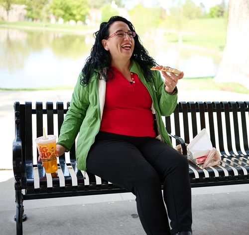 a woman eating pizza on a bench