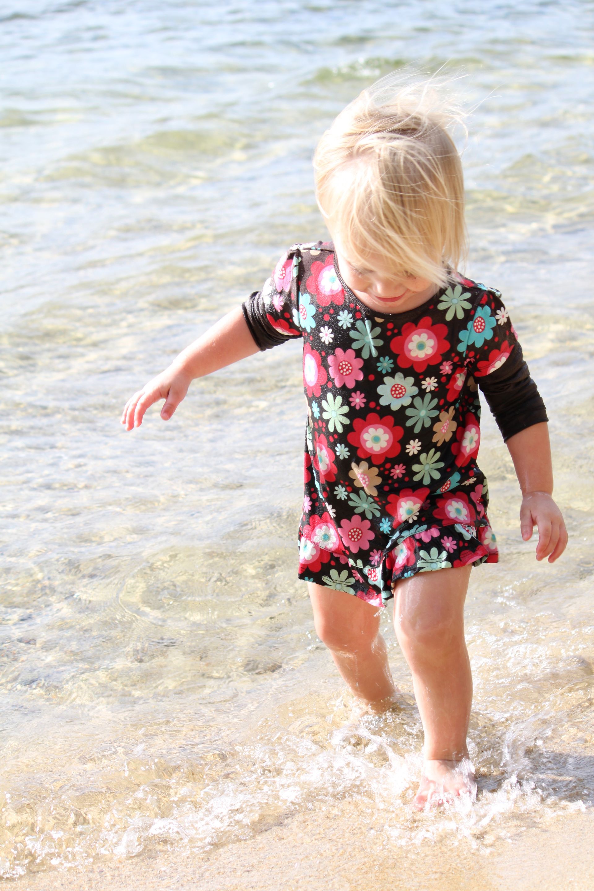 A little girl walks in the water on the beach.