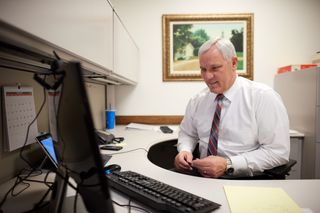 A man sits and works in an office. He is on a computer. He is in an employment office.