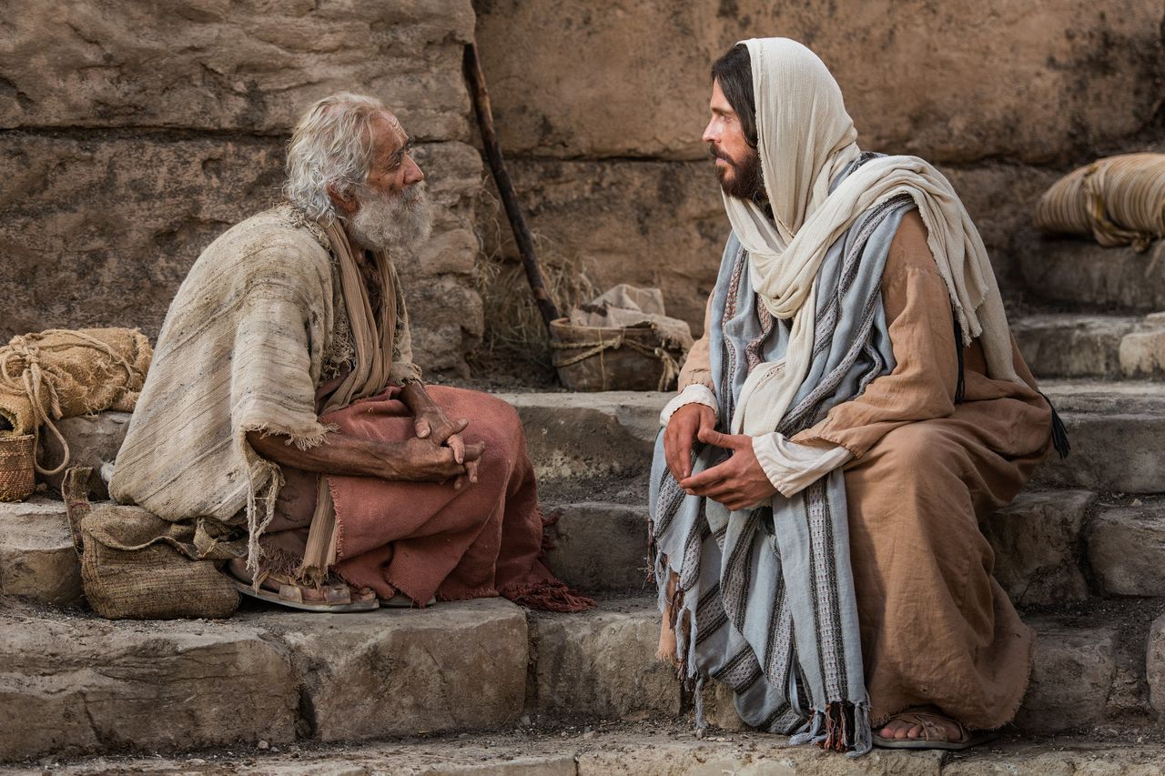 Jesus Christ sits with a man at the pools of Bethesda speaking with a man whom He healed