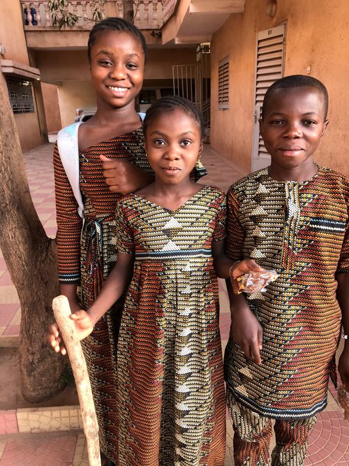 three siblings standing together in beautiful patterned clothes