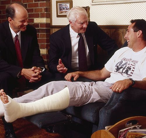 two men visiting a man with an injured leg