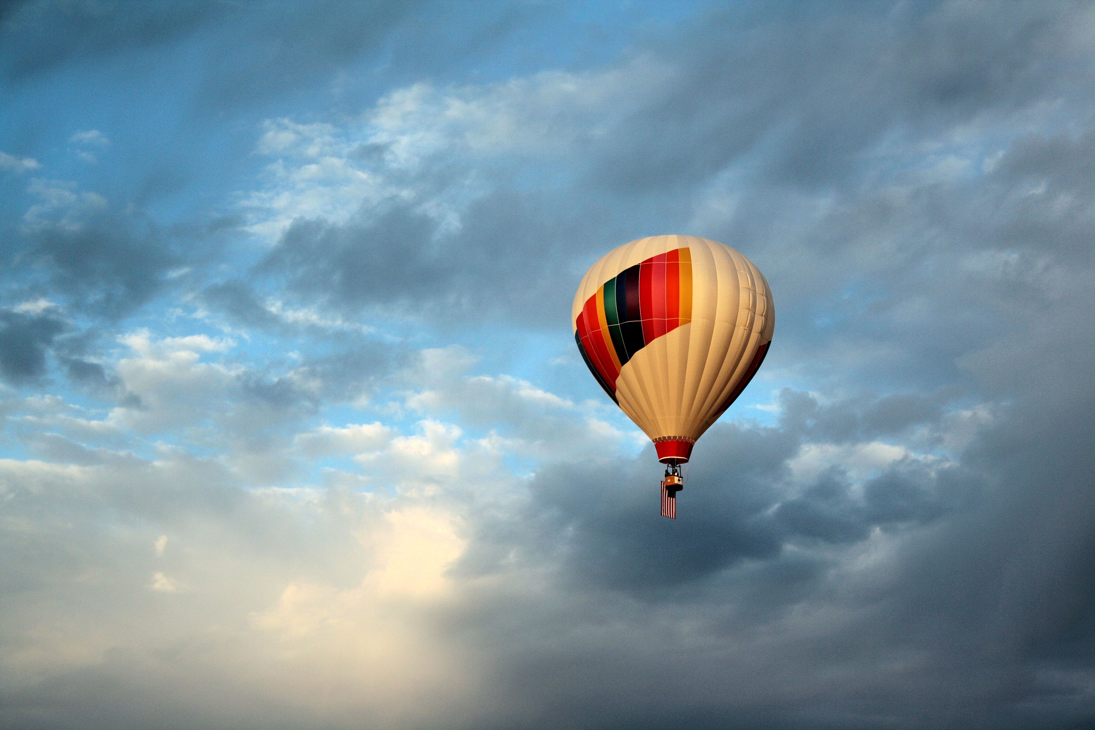 A hot air balloon is seen flying through white and gray clouds, with a blue sky in the background.