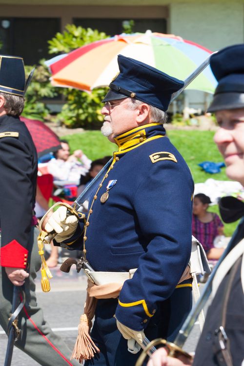 A soldier wearing a blue uniform and hat, standing outside between two other soldiers in a reenactment of the Mormon Battalion.