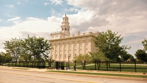 A side view of the Nauvoo Illinois Temple and grounds on a sunny day, with the temple’s black fence surrounding the perimeter of the grounds.