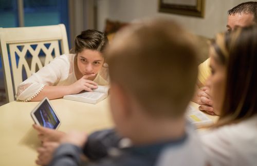 A family sits around a table studying the scriptures.  Some have books and some have IPads - in Florida.