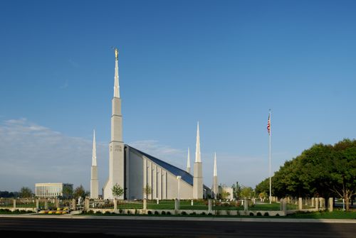 The front of the Boise Idaho Temple as seen from across the street on a sunny day, with the American flag flying on the grounds.