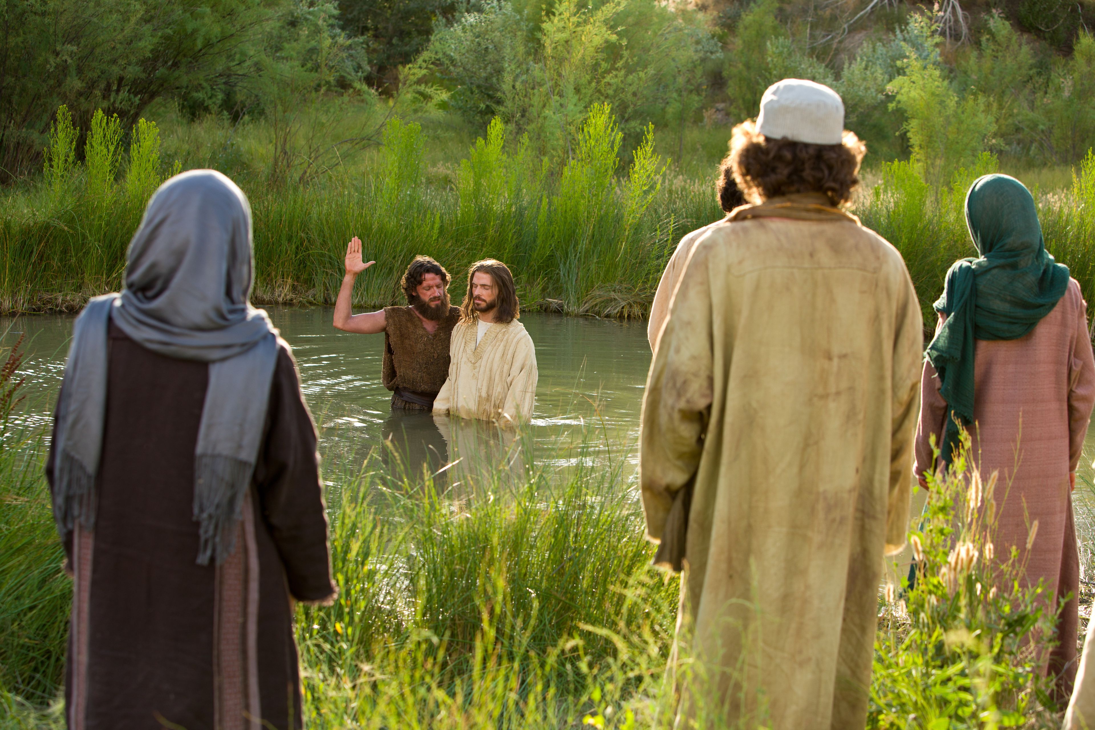 John the Baptist baptizes the Savior in the River Jordan as others look on.