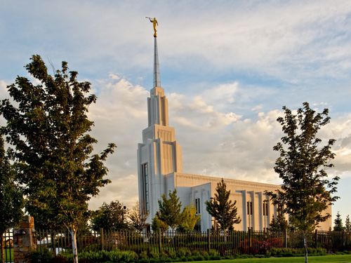 A side view of the Twin Falls Idaho Temple in the evening, with the grounds, trees, and fence.