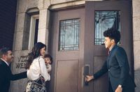 Un hombre sujeta la puerta para que una familia joven entre en un edificio de la Iglesia