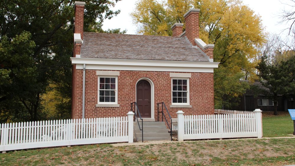 Small brick home with chimneys on either side and stairs leading up to the front door.