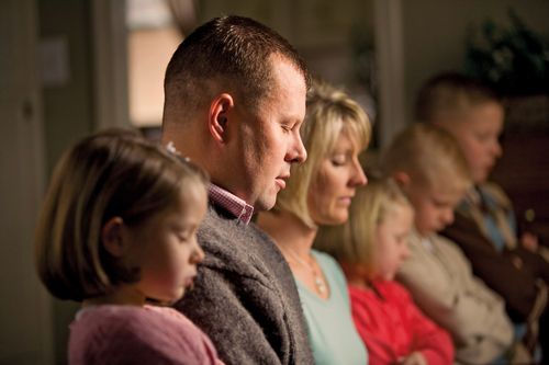 A family kneel in a row while the father closes his eyes and prays.
