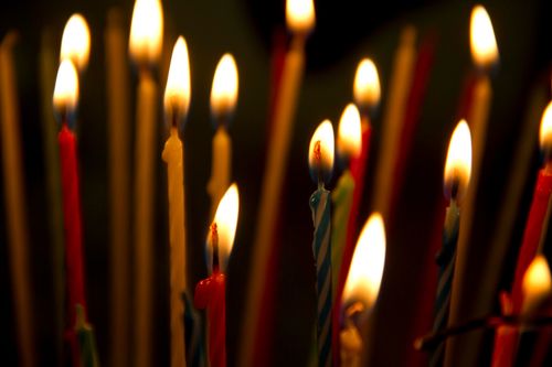 A close-up view of red, yellow, blue, and green birthday candles burning in the dark.