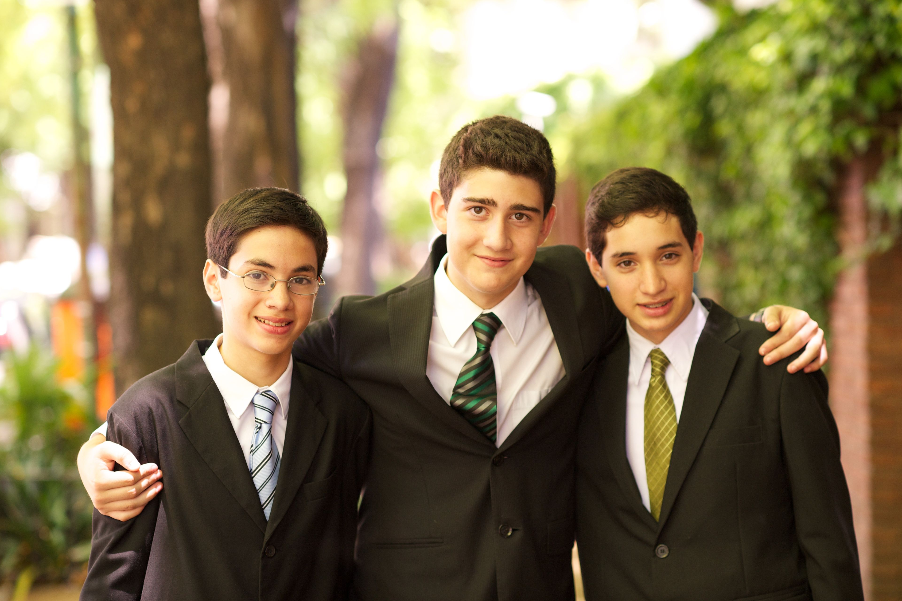 A portrait of three young men in suits and ties, standing side by side and smiling.