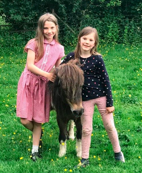 Vivie and Lucia Jenkins (sisters) smile as they stand next to a miniature pony.