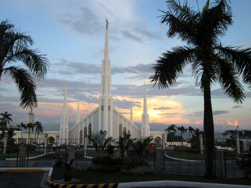 The entrance and grounds view of the Manila Philippines Temple, with palm trees surrounding and the late evening sky coloring the clouds.