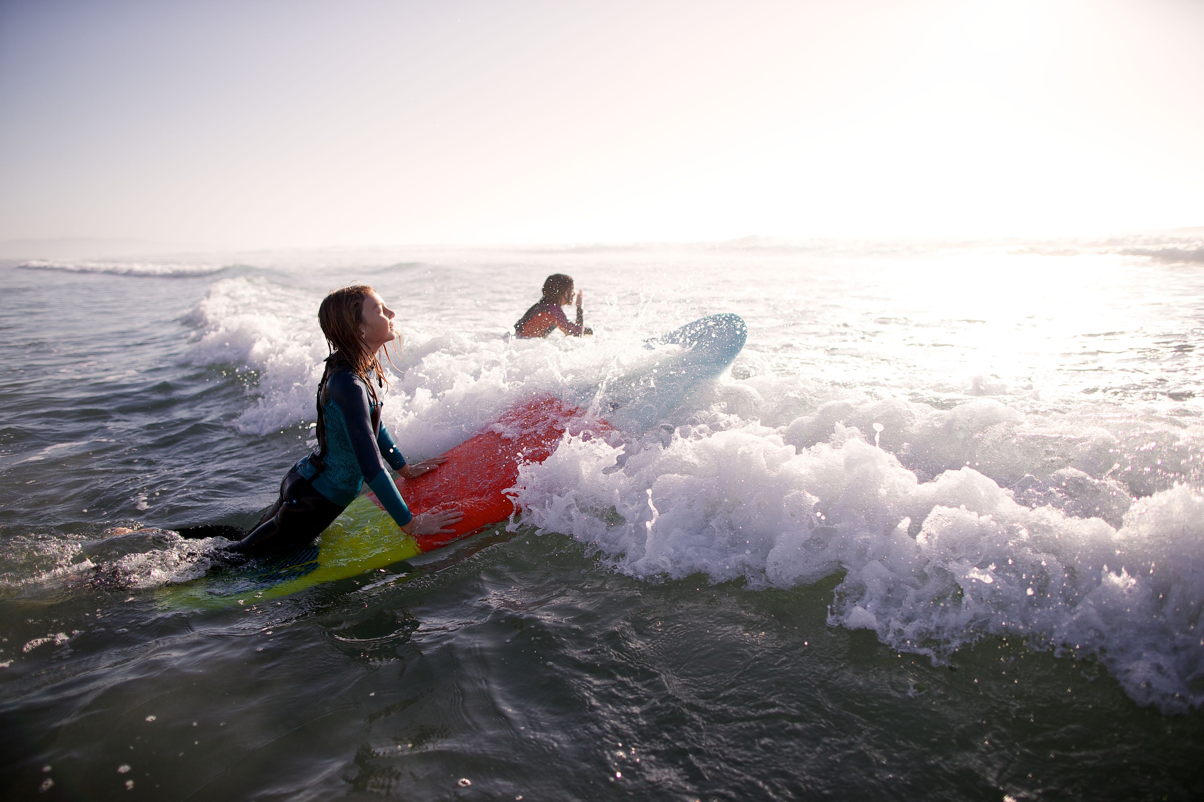 Two women paddle out on surfboards.