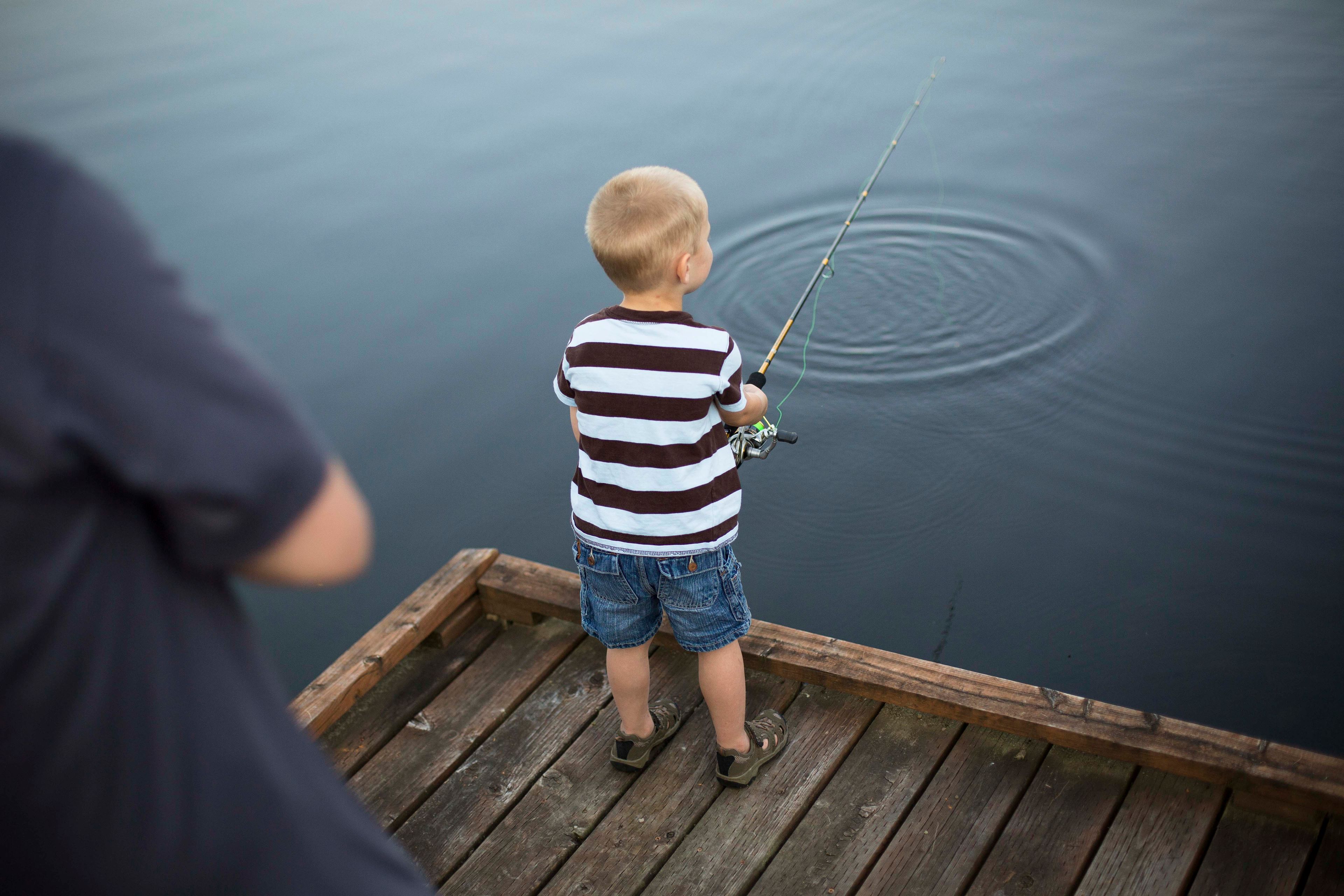 A little boy fishes with his father.  