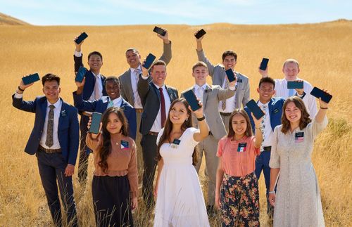 group of missionaries stand together in a field, each holding a cell phone